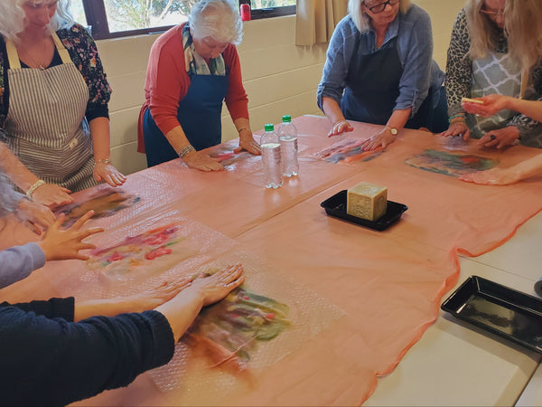 Group of people working on art projects at a table with aprons on
