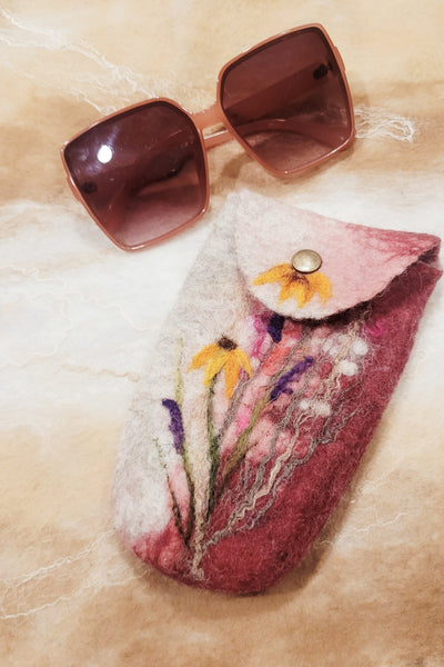 Sunglasses and a pink felted pouch with floral design on a beige surface