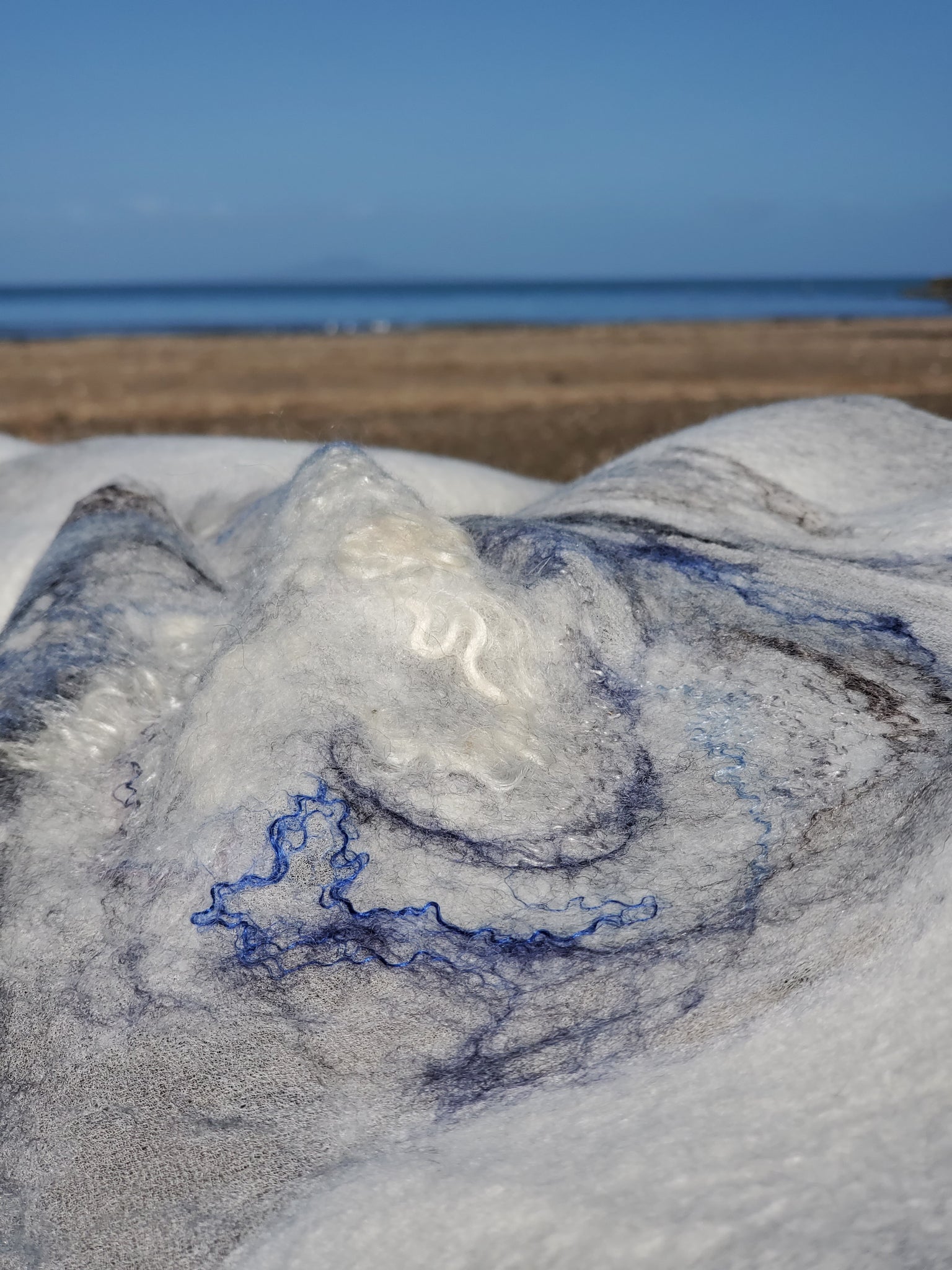 White Handmade shawl nunofelting lies on the beach