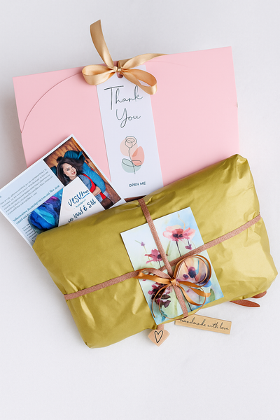 a pink box with a gold ribbon, a yellow gift bag with a floral design, and a card with a photo and a heart-shaped tag.