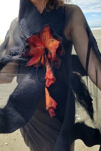 A person outdoors on a beach wearing a sheer black wrap with a large red and orange flower appliqué on the chest.