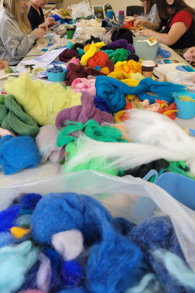 People working with colourful wool at a table in a workshop setting.