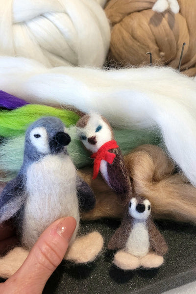 Hand holding a felted animal toy surrounded by wool and other toys.