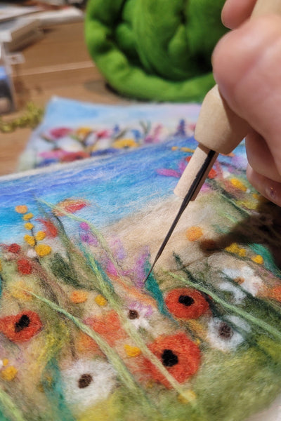 Needle felting, painting a colourful floral scene on fabric with wool.