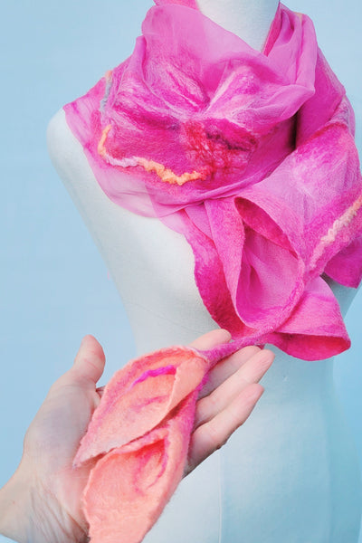 Mannequin wearing a bright pink scarf with gradient ends, held by a hand against a light blue background.