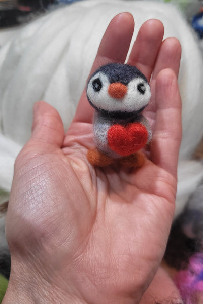 Hand holding felted penguin toy against a blurred background