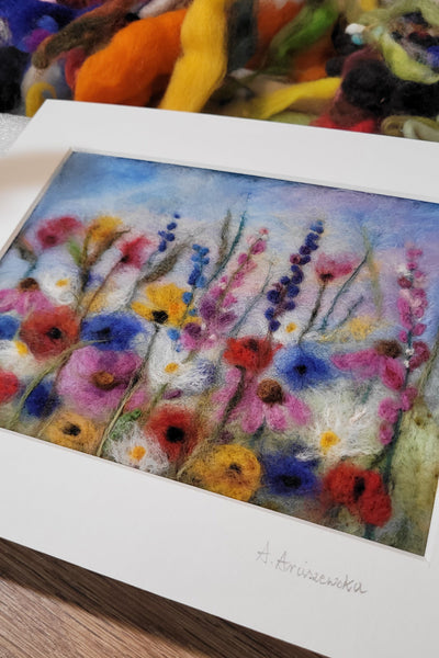 Colorful floral painting on a white card with a wooden surface and colorful fabric in the background.