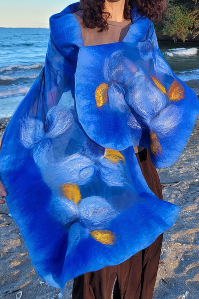 Crafted merino wool and silk scarf in bright blue with  flowers design woth golden accents, worn on a beach in New Zealand. VESU versatile elegance. 