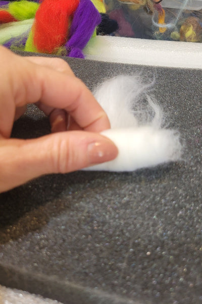 Hand holding a piece of white wool against a textured grey background.