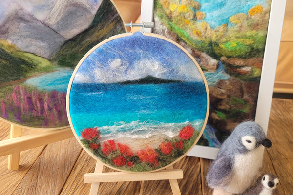 Handmade wool painting in an embroidery hoop with a scenic landscape design on a wooden shelf.