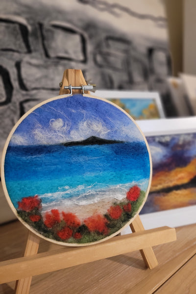 Round merino wool artwork with blue, red, and white colours on a wooden easel.