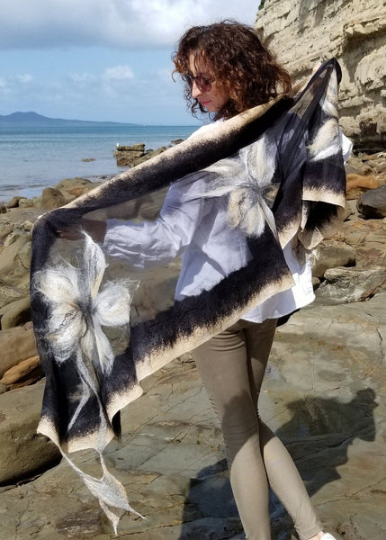 nunofelting shawl with big flowers in beige, cream and black. Women with shawl and sea background.